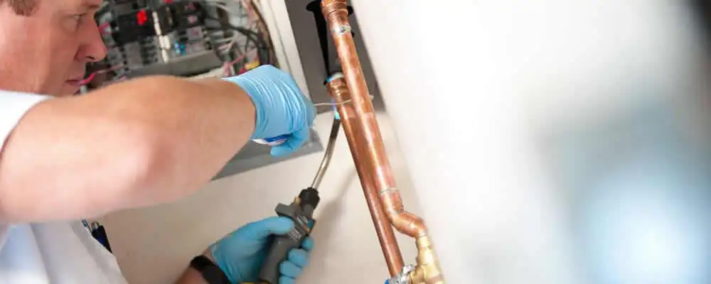 Water heater repair technician testing copper pipe connections and controls in Glendale, AZ